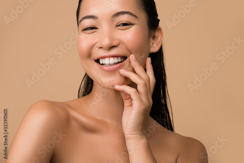 smiling beautiful naked asian girl touching face isolated on beige