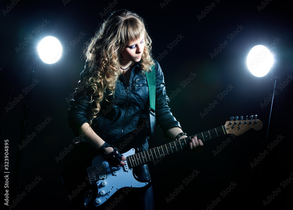 Fototapeta premium Girl guitarist with black and white guitar. Behind two spotlights. background is black