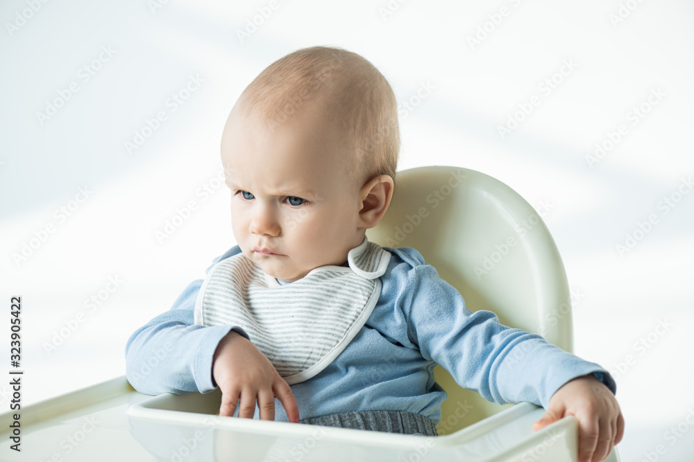 Pensive baby boy sitting on feeding chair on white background Pensive baby boy sitting on feeding chair on white background