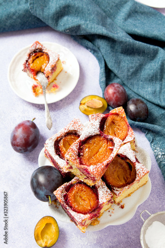 Tasty plum cake with pieces of fruit and powdered sugar on a light background