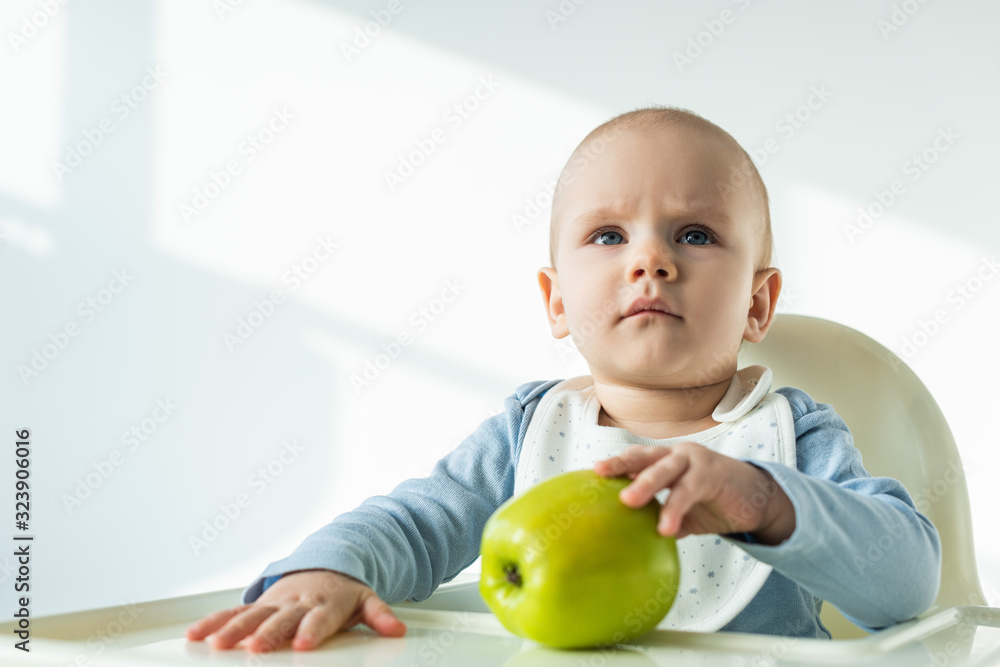 Cute baby boy touching green apple on table of feeding chair on white background Cute baby boy touching green apple on table of feeding chair on white background