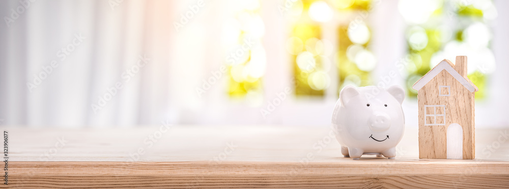 Piggy bank and model house on a bright interior room background - obrazy, fototapety, plakaty 