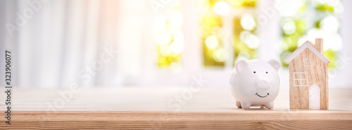 Piggy bank and model house on a bright interior room background