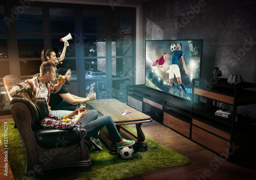 Group of friends watching TV, match, championship, sport games. Emotional men and women cheering for favourite football, soccer team, look on fighting for ball. Concept of friendship, emotions. photo