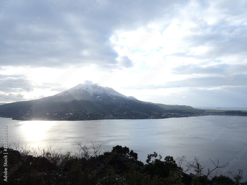 海に反射する太陽の輝きと桜島の初雪