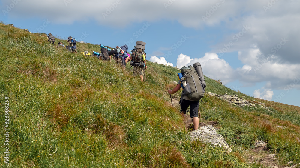 Obraz premium Tourists with hiking backpacks walk along a mountain trail. Background illustrating a healthy lifestyle.