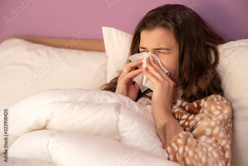 Young woman with cold blowing her nose in bed.