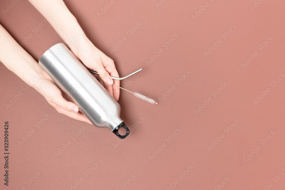 Female hands hold metal bottle, tube and cleaning brush. Minimalistic concept with copy space on brown background. Female hands hold metal bottle, tube and cleaning brush. Minimalistic concept with copy space on brown background.