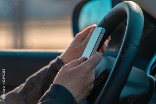 Fotografie Businesswoman driving car and text messaging on mobile phone