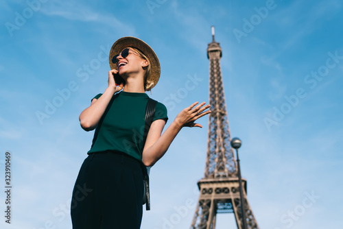 Excited Caucasian female traveller enjoying smartphone conversation with friend during holidays time for visit romantic showplace, joyful woman in sunglasses and hat calling via mobile network app
