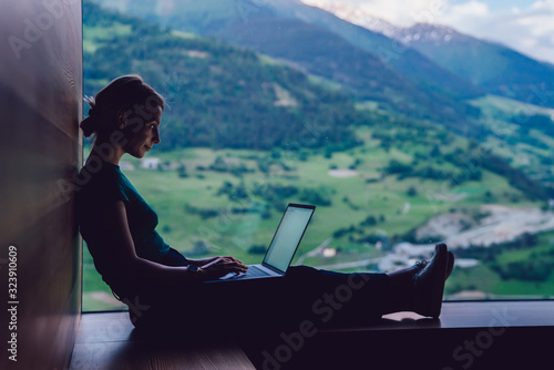 Skilled female digital nomad working remotely creating trip guide to high mountains for share to followers in social networks connected to 4g internet, skilled freelancer typing text on laptop photo
