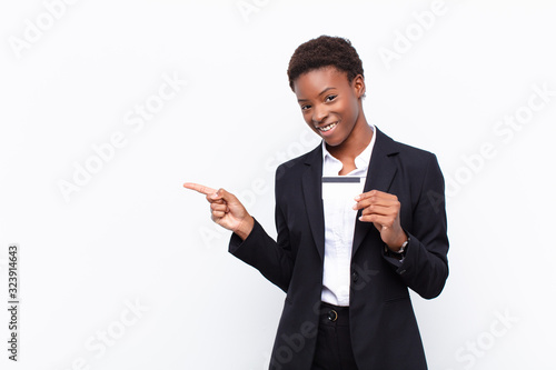 young pretty black womanlooking excited and surprised pointing to the side and upwards to copy space holding a credit card photo