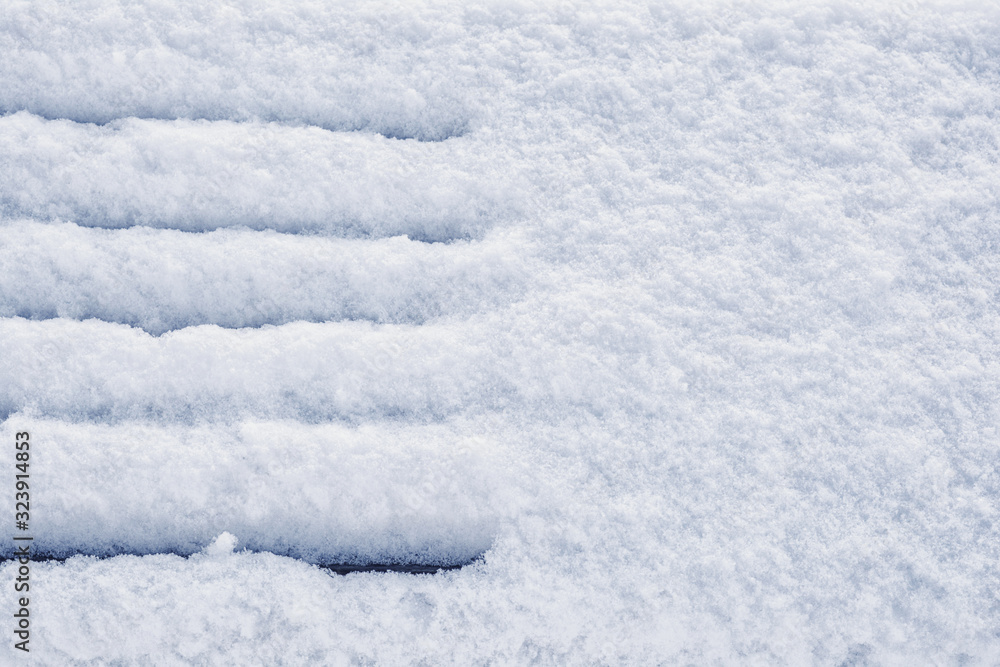 Snow covered wooden bench in winter park on fluffy white snow background