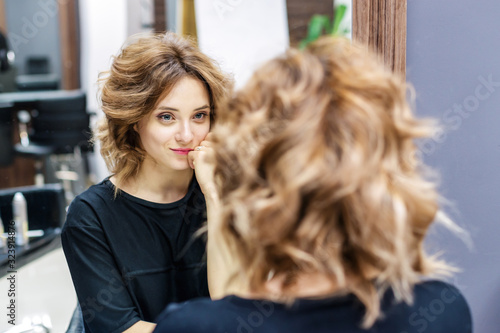 Young woman with hairstyle looking in the mirror in beauty salon.
