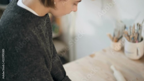 Potterry woman making clay blank for the ceramics work. Handheld shot from face till hands. Working on the table. Slowmotion. photo