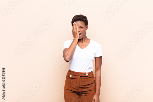 young pretty black womanlooking sleepy, bored and yawning, with a headache and one hand covering half the face photo