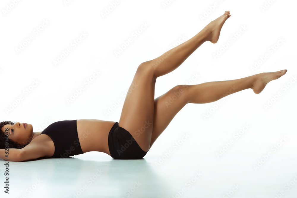 Anti-cellulite and epilation. Slim tanned woman's body on white studio background. African-american model with well-kept shape and skin. Beauty, self-care, weight loss, fitness, slimming concept. Anti-cellulite and epilation. Slim tanned woman's body on white studio background. African-american model with well-kept shape and skin. Beauty, self-care, weight loss, fitness, slimming concept.