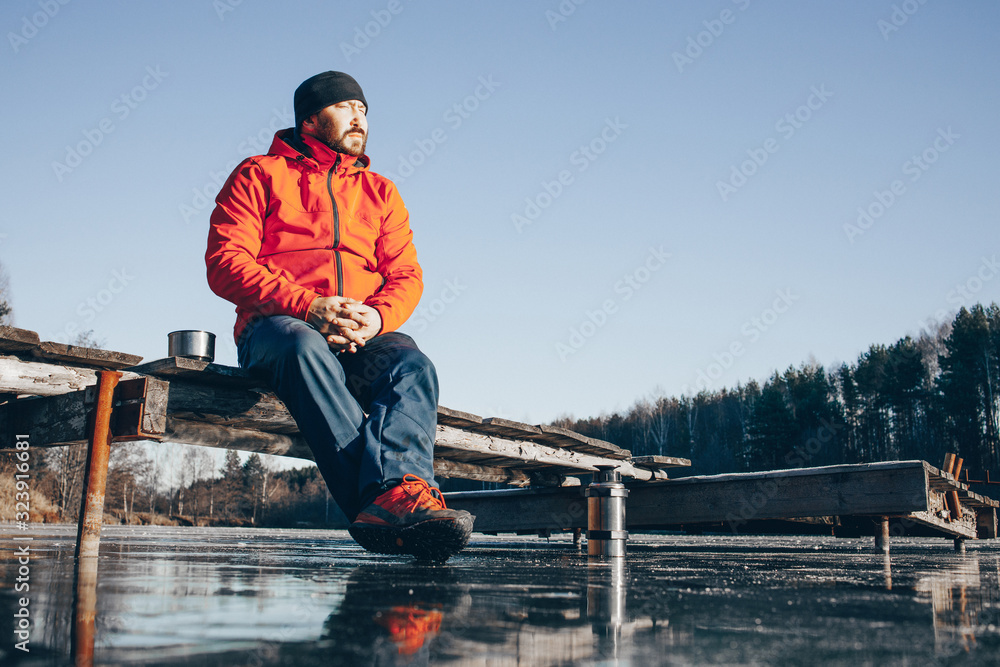 A lone tramp traveler stands on ice and drinks tea from a thermos. A lone tramp traveler stands on ice and drinks tea from a thermos.
