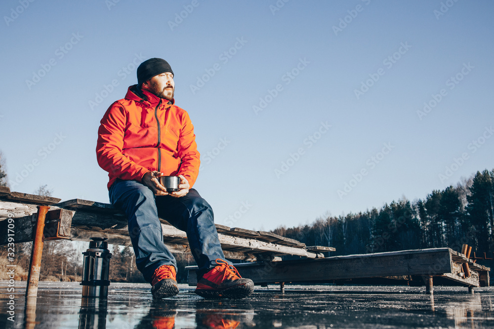 A lone tramp traveler stands on ice and drinks tea from a thermos. A lone tramp traveler stands on ice and drinks tea from a thermos.