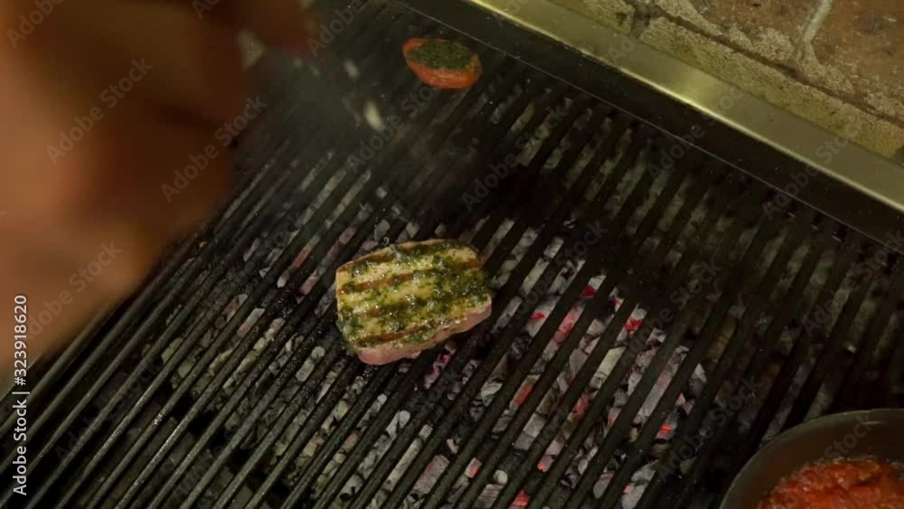 Hand sprinkling salt on piece of tuna on grill. Handheld, top view Hand sprinkling salt on piece of tuna on grill. Handheld, top view