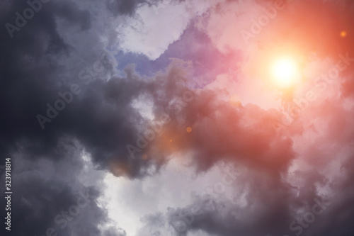 Dramatic storm dark grey cumulus clouds with orange sun and sunlight 