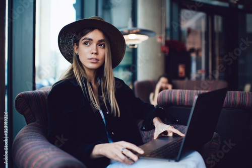 Thoughtful stylish woman looking away while working on laptop in cafe