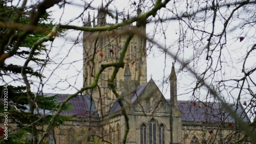 Smooth drifting shot, looking through tree branches towards impressive tower of Wells Cathedral, in England's smallest city photo