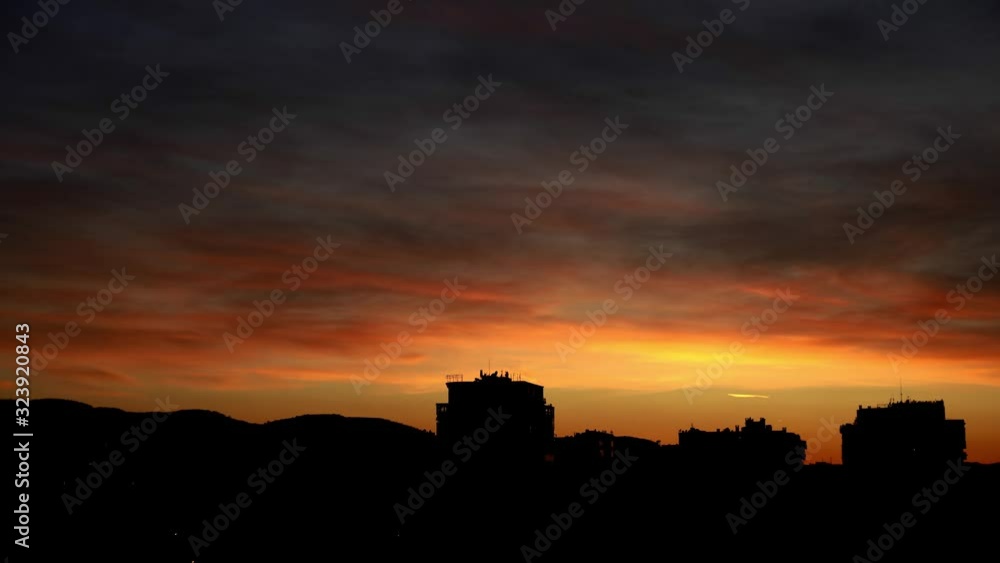 Silhouette of city buildings at dramatic sunset with glowing yellow red sky under dark grey clouds moving fast Silhouette of city buildings at dramatic sunset with glowing yellow red sky under dark grey clouds moving fast