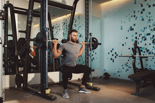 Young handsome man doing squat exercises at the gym on a squat machine