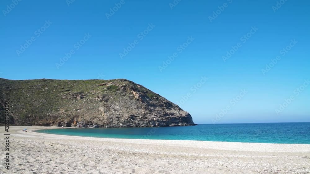 Wide-angle view on a calm, blue-sky day looking out at the Aeagean sea, the beach, and cliffs from the the beautiful hidden gem, Zorgos Beach on the Greek island of Andros. Wide-angle view on a calm, blue-sky day looking out at the Aeagean sea, the beach, and cliffs from the the beautiful hidden gem, Zorgos Beach on the Greek island of Andros.