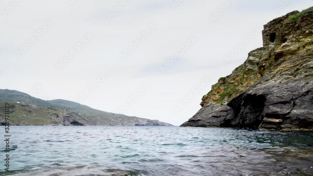 Gentle waves lap against the cliffs and rocky coast of the Greek island of Andros. Gentle waves lap against the cliffs and rocky coast of the Greek island of Andros.