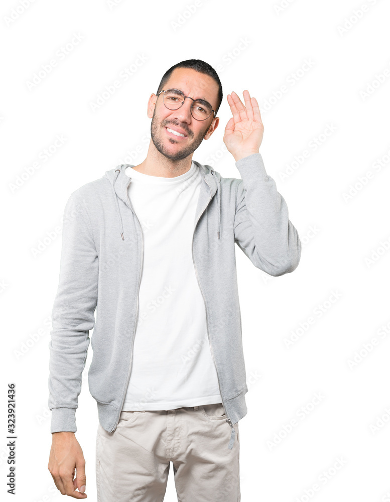 Happy young man smiling and making a gesture of trying to hear something Happy young man smiling and making a gesture of trying to hear something