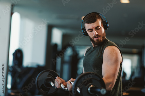 Young bearded man doing biceps exercises in gym with barbell