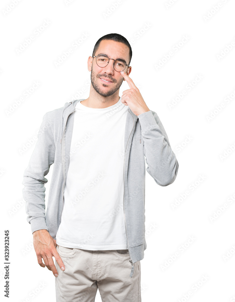 Fototapeta premium Friendly young man making a gesture of being careful with his hand pointing at his eye