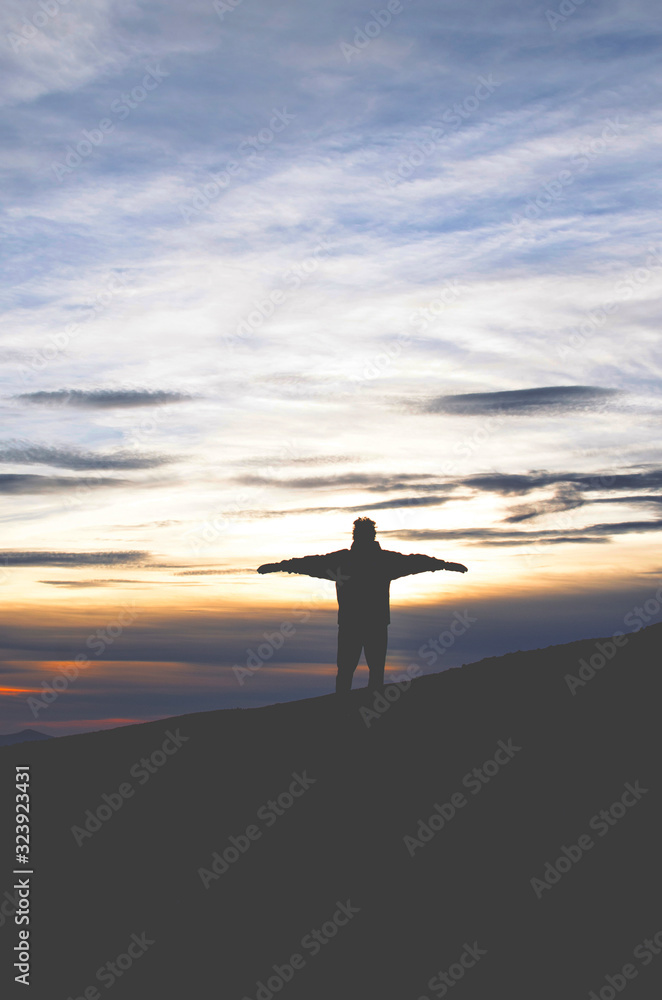 Feeling of freedom Man standing with arms outstretched on top of a mountain in front of a sunset landscape