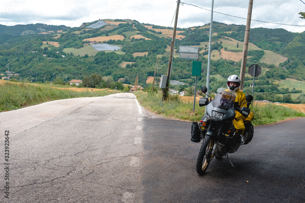 Motorcyclist traveler girl wearing yellow raincoat and sitting in a motorcycle saddle. Motorbike on mountain road. Extreme travel tour. Biker equipment. Copy space.