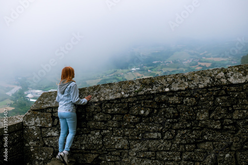 A girl dressed in a denim jacket and blue pants, posing against the backdrop of a medieval fortification. travel and vacation concept. San Marino first tower: la Rocca or Guaita