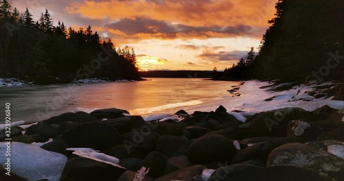 Sunset at the mouth of a Beautiful rocky and snow covered cove surrounded by dead fall pine trees in rural Nova Scotia, Canada photo