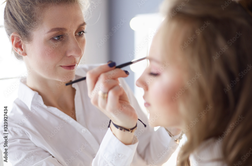 Young beautiful bride applying wedding make-up by professional make-up artist Young beautiful bride applying wedding make-up by professional make-up artist