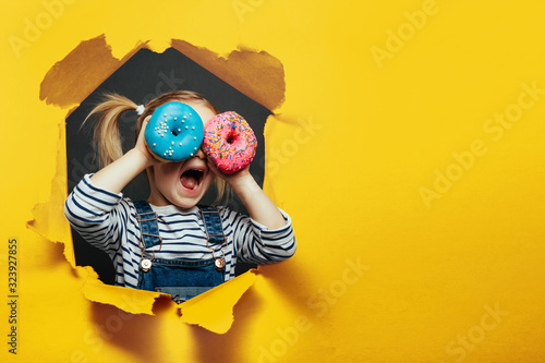 Happy cute boy is having fun played with donuts on black background wall.