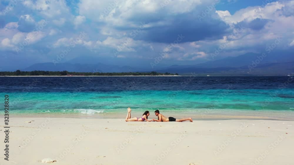 Young couple lying on white sand of exotic beach alongside blue azure sea on a beautiful cloudy sky background in Indonesia Young couple lying on white sand of exotic beach alongside blue azure sea on a beautiful cloudy sky background in Indonesia