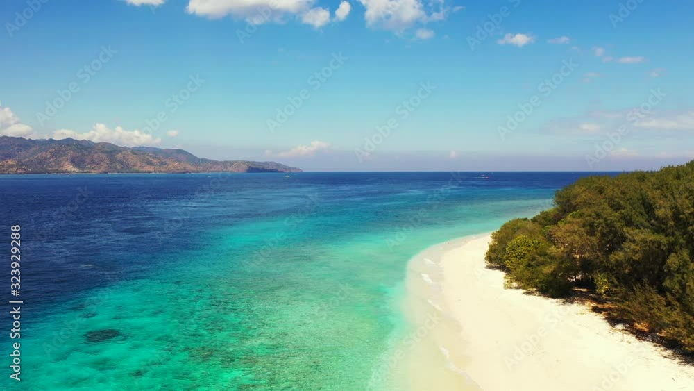 Pristine white sandy beach washed by crystal calm water of turquoise lagoon and blue sea on tropical island with lush vegetation in Bali Pristine white sandy beach washed by crystal calm water of turquoise lagoon and blue sea on tropical island with lush vegetation in Bali