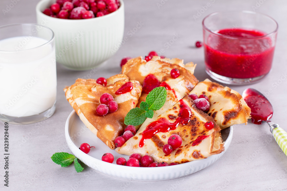Thin pancakes or crepes on a ceramic plate with jam and frozen berries, mint Thin pancakes or crepes on a ceramic plate with jam and frozen berries, mint