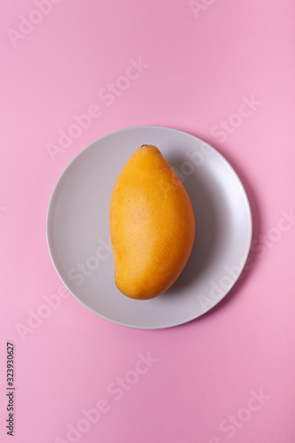 Fresh yellow mango on a grey plate and pink background. Ripe exotic fruit. Pastel background. 
