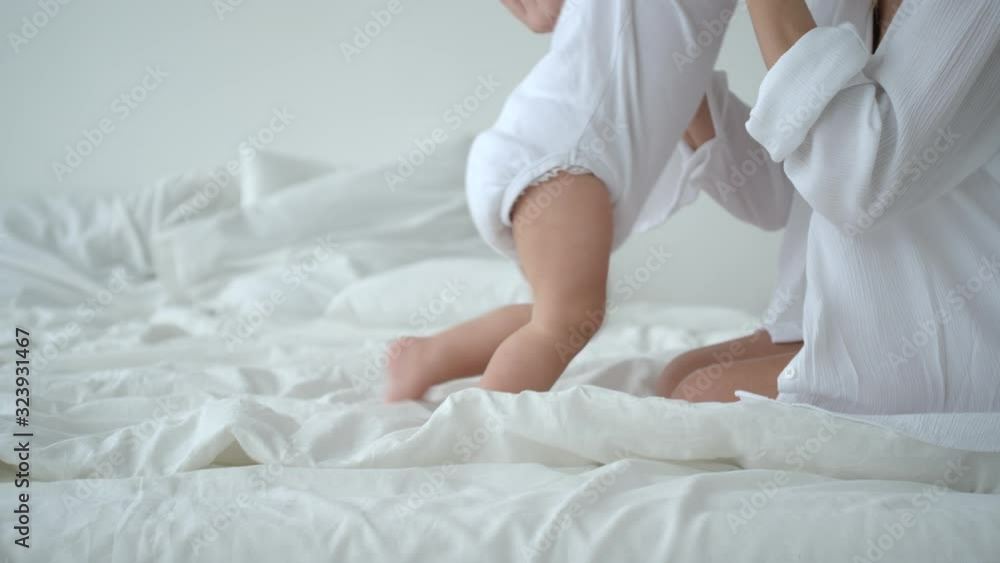 Mother Helps Her Cute Infant Baby To Make First Steps On Bed Mother Helps Her Cute Infant Baby To Make First Steps On Bed
