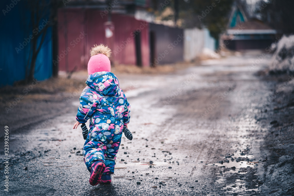 Cheerful child in winter clothes walks on road on spring day. Cheerful child in winter clothes walks on road on spring day.
