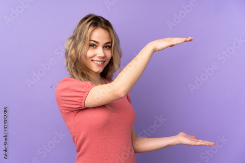 Teenager Russian girl isolated on purple background holding copyspace to insert an ad