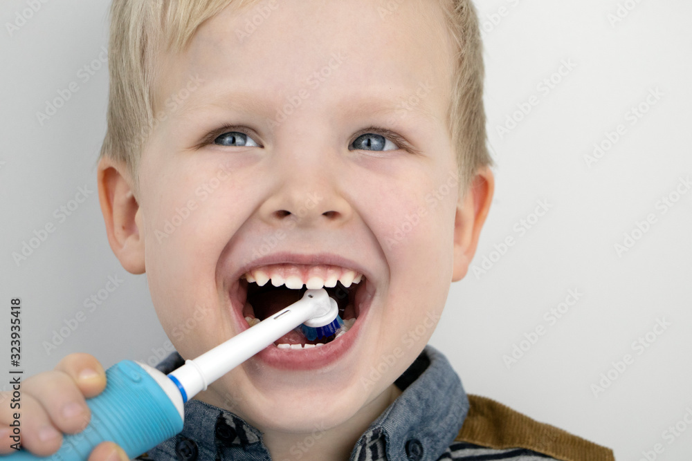 Four year old child brushes his teeth with an electric brush. The boy on a white background laughs and holds a toothbrush. The concept of baby teeth and oral hygiene Four year old child brushes his teeth with an electric brush. The boy on a white background laughs and holds a toothbrush. The concept of baby teeth and oral hygiene