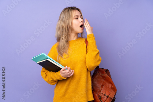 Teenager Russian student girl isolated on purple background yawning and covering wide open mouth with hand