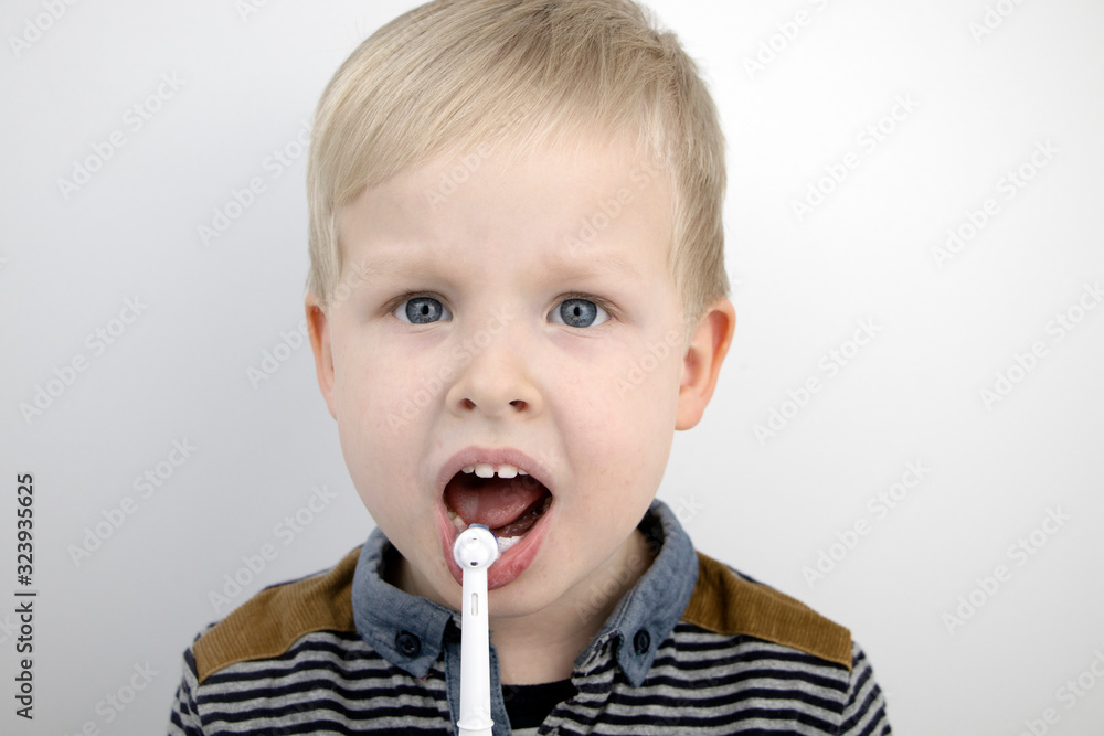Four year old child brushes his teeth with an electric brush. The boy on a white background laughs and holds a toothbrush. The concept of baby teeth and oral hygiene Four year old child brushes his teeth with an electric brush. The boy on a white background laughs and holds a toothbrush. The concept of baby teeth and oral hygiene